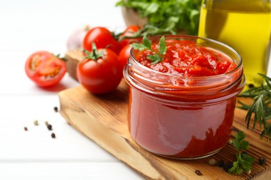 Photo of Homemade tomato sauce in jar and fresh ingredients on white wooden table, closeup