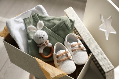 Box with baby clothes, shoes and toy on chair indoors
