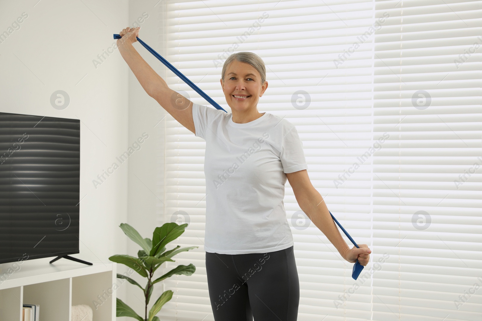 Photo of Senior woman doing exercise with fitness elastic band at home