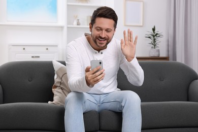 Photo of Happy man greeting someone during video chat via smartphone at home