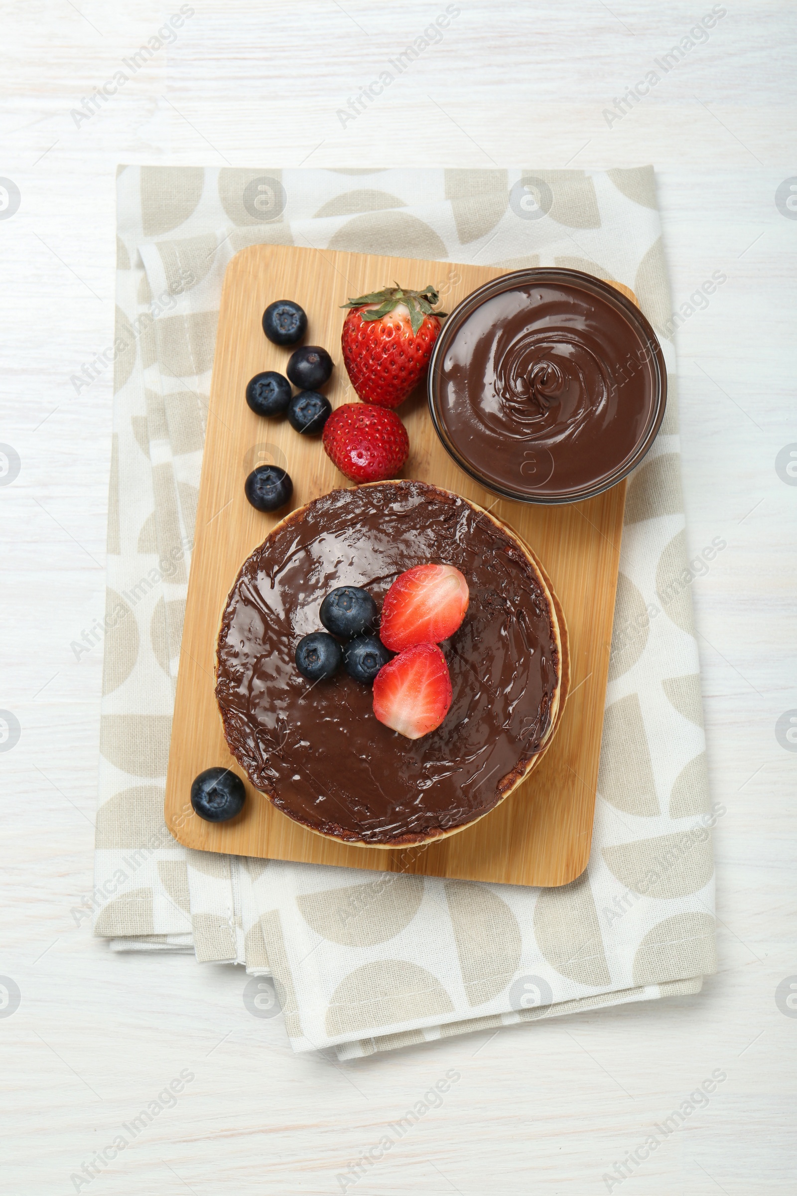 Photo of Tasty pancakes with chocolate paste and berries on white wooden table, top view