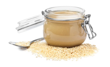 Photo of Tasty sesame paste in jar, spoon and seeds on white background