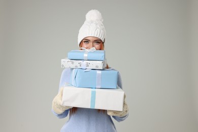 Photo of Young woman in hat and sweater with Christmas gifts on light grey background