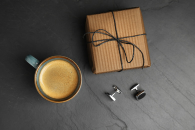 Cup of coffee, gift box and cuff links on black table, flat lay. Happy father's day