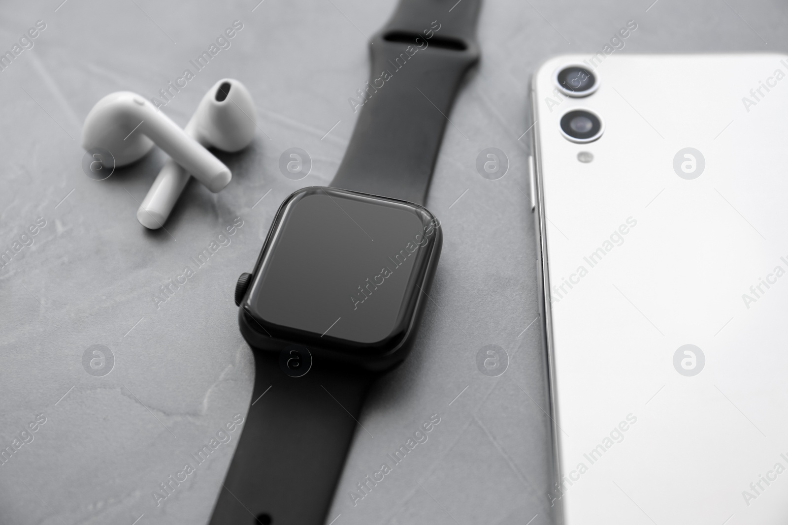 Stylish smart watch, phone and earphones on grey stone table, closeup Photo of Stylish smart watch, phone and earphones on grey stone table, closeup