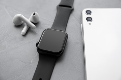 Photo of Stylish smart watch, phone and earphones on grey stone table, closeup