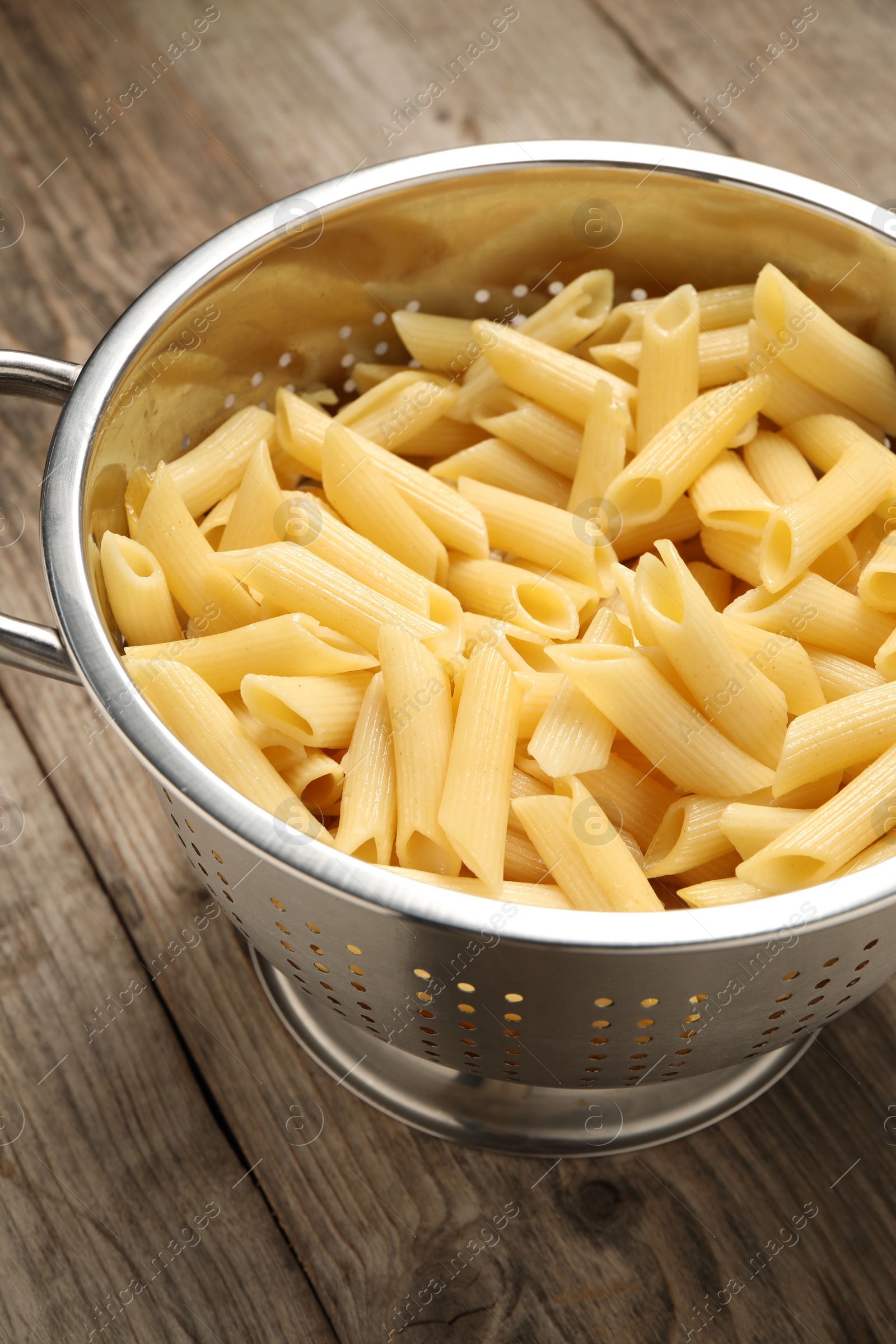 Photo of Delicious penne pasta in colander on wooden table, closeup