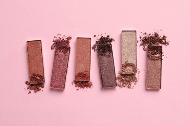 Photo of Different crushed eye shadows on pink background, flat lay. Professional makeup product