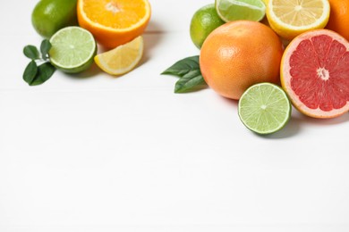 Photo of Different fresh citrus fruits and leaves on white wooden table. Space for text