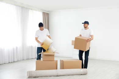 Moving service employees with cardboard boxes in room