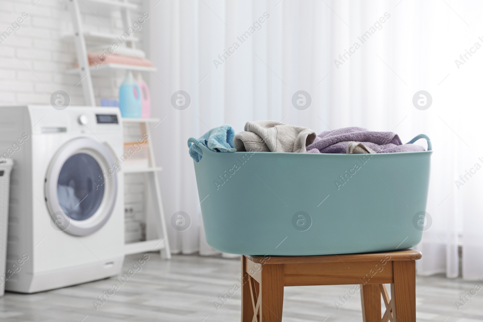 Photo of Plastic basket with dirty towels on table in laundry room, space for text