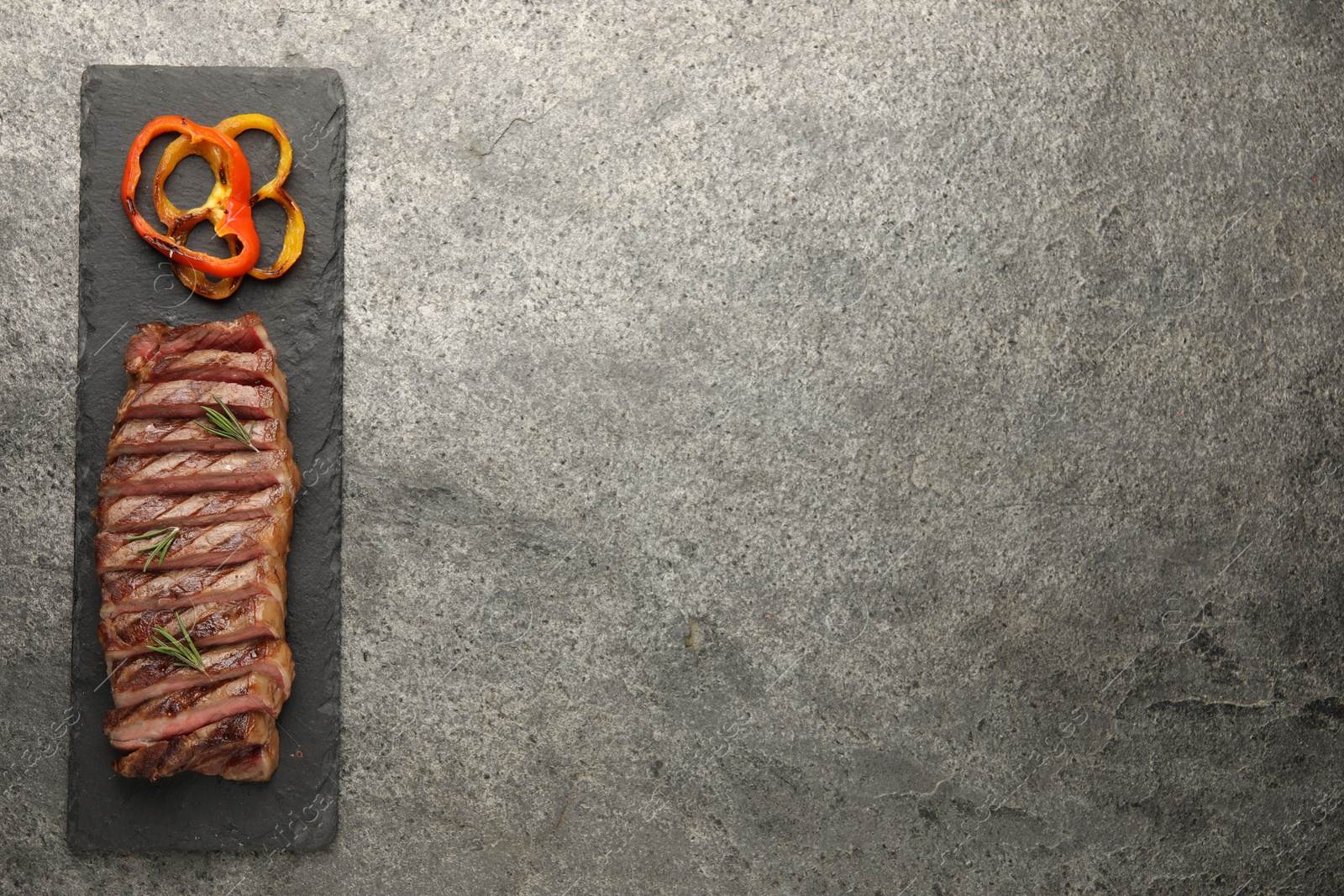 Photo of Delicious grilled beef steak with spices on gray table, top view. Space for text