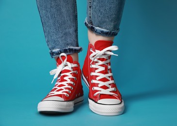 Woman wearing pair of new stylish sneakers on light blue background, closeup