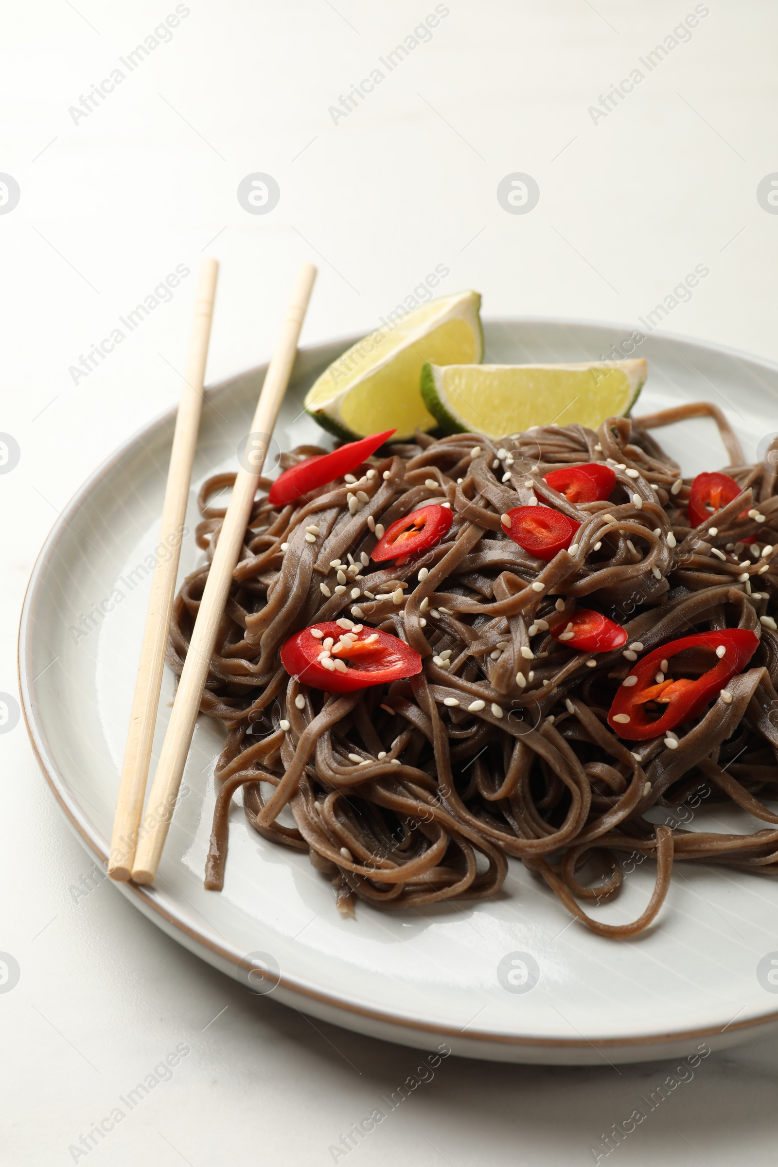 Photo of Tasty buckwheat noodles (soba) with chili pepper, lime and chopsticks on white table