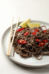 Photo of Tasty buckwheat noodles (soba) with chili pepper, lime and chopsticks on white table