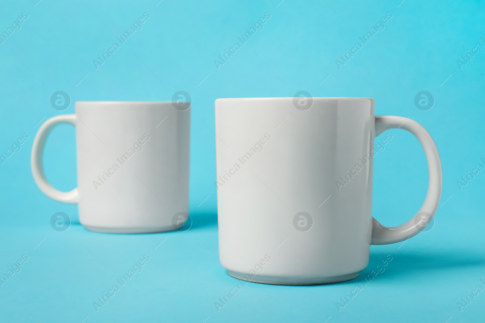 Photo of Two white ceramic mugs on light blue background