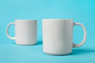 Two white ceramic mugs on light blue background