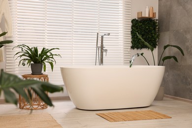 Green artificial plants and tub near window in bathroom
