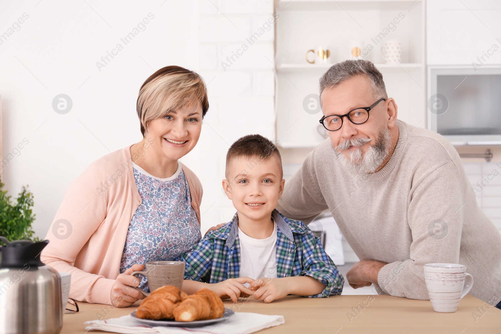 Photo of Happy senior couple having breakfast with little grandson at home