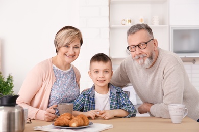 Happy senior couple having breakfast with little grandson at home