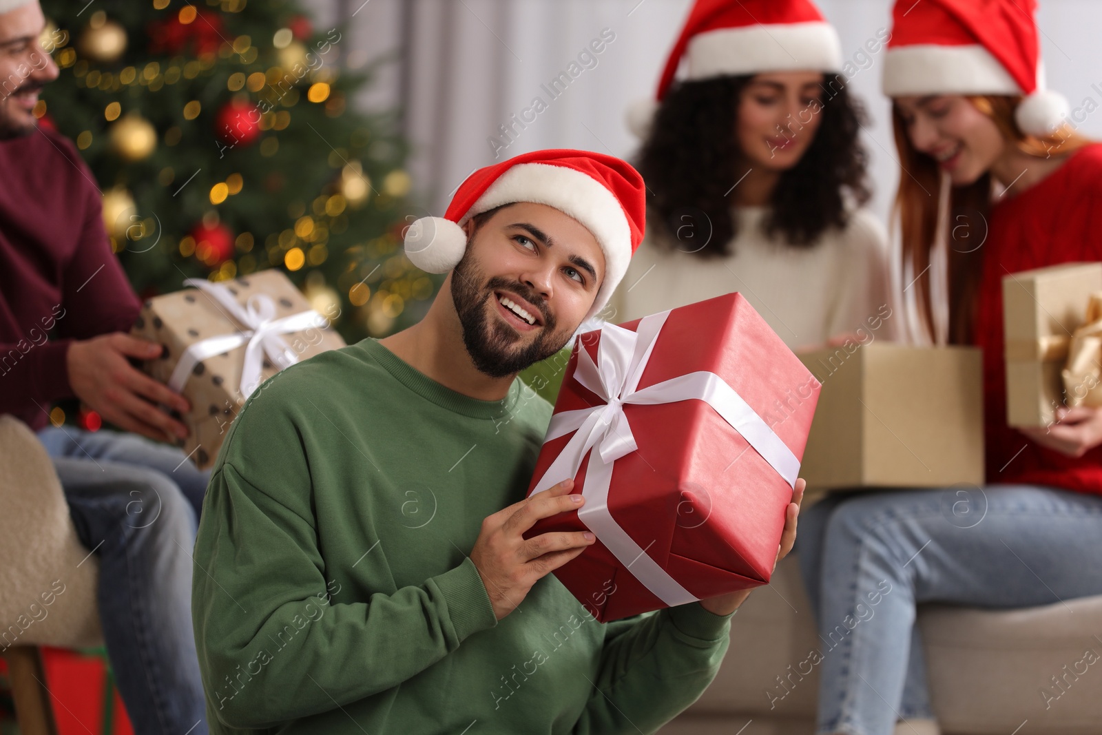 Photo of Christmas celebration in circle of friends. Happy young man with gift box at home, selective focus