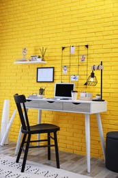 Photo of Stylish home office interior with comfortable workplace near yellow brick wall