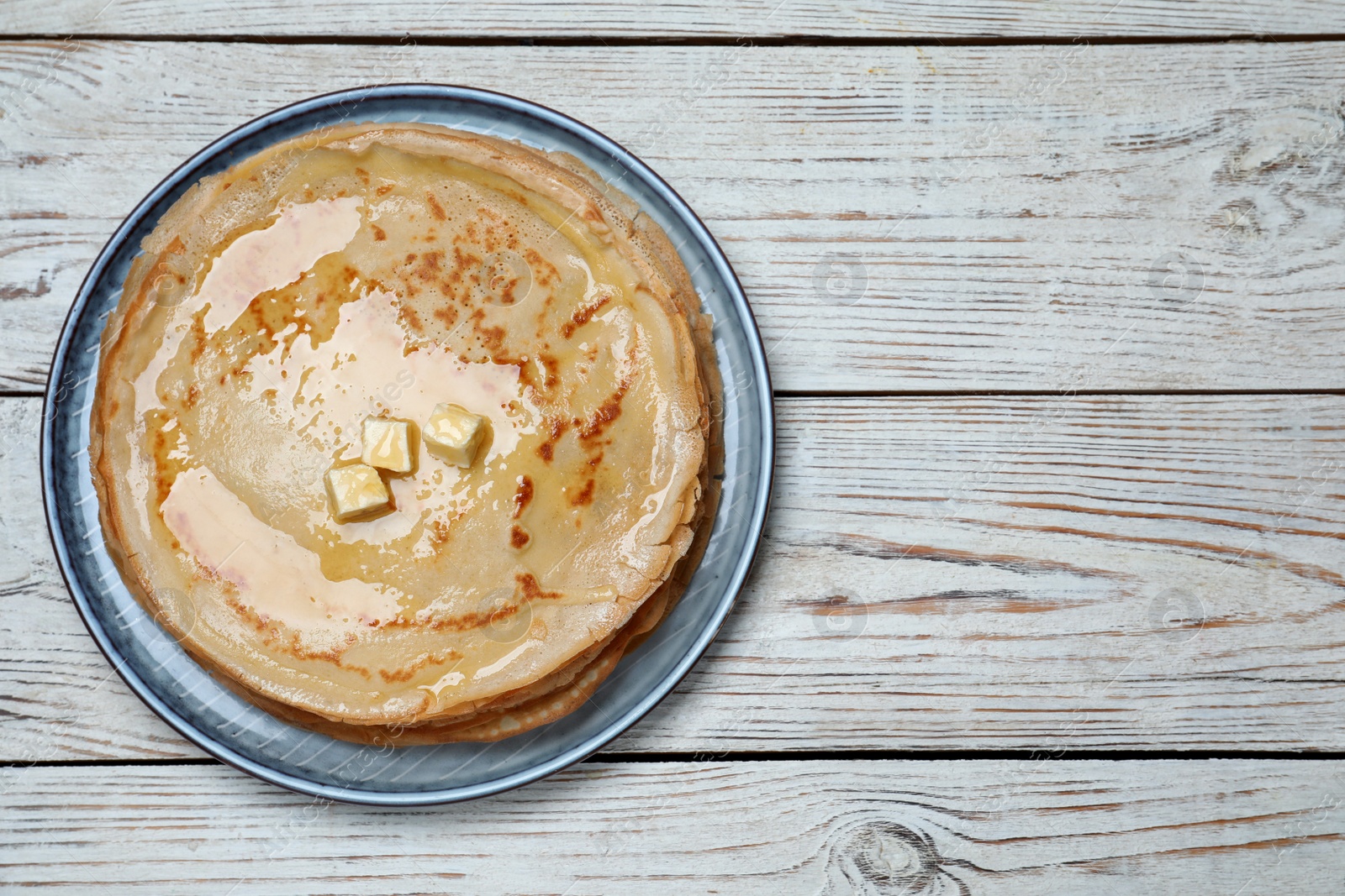 Photo of Delicious crepes with melting butter on white wooden table, top view. Space for text