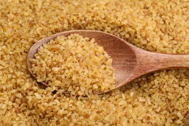 Photo of Wooden spoon on pile of uncooked bulgur, closeup