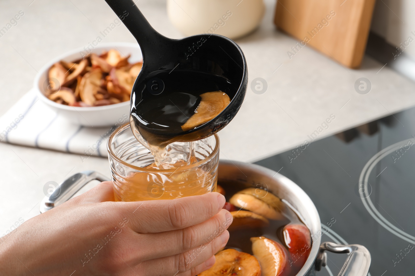 Photo of Woman pouring compot into glass near stove, closeup