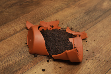 Broken terracotta flower pot with soil on wooden floor