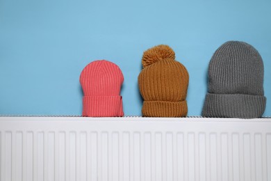 Modern radiator with knitted hats near light blue wall indoors
