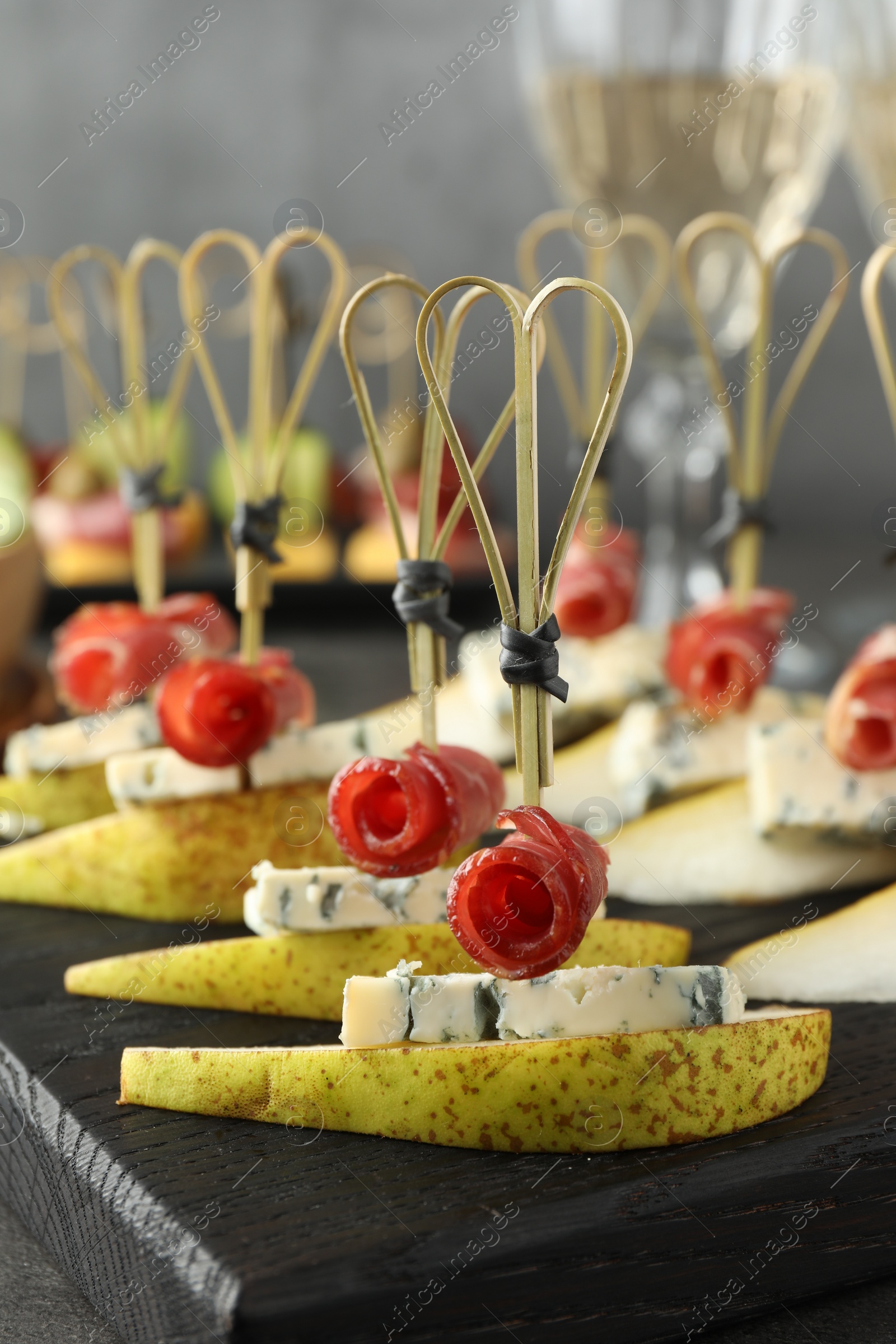 Photo of Tasty canapes with pears, blue cheese and prosciutto on grey table, closeup