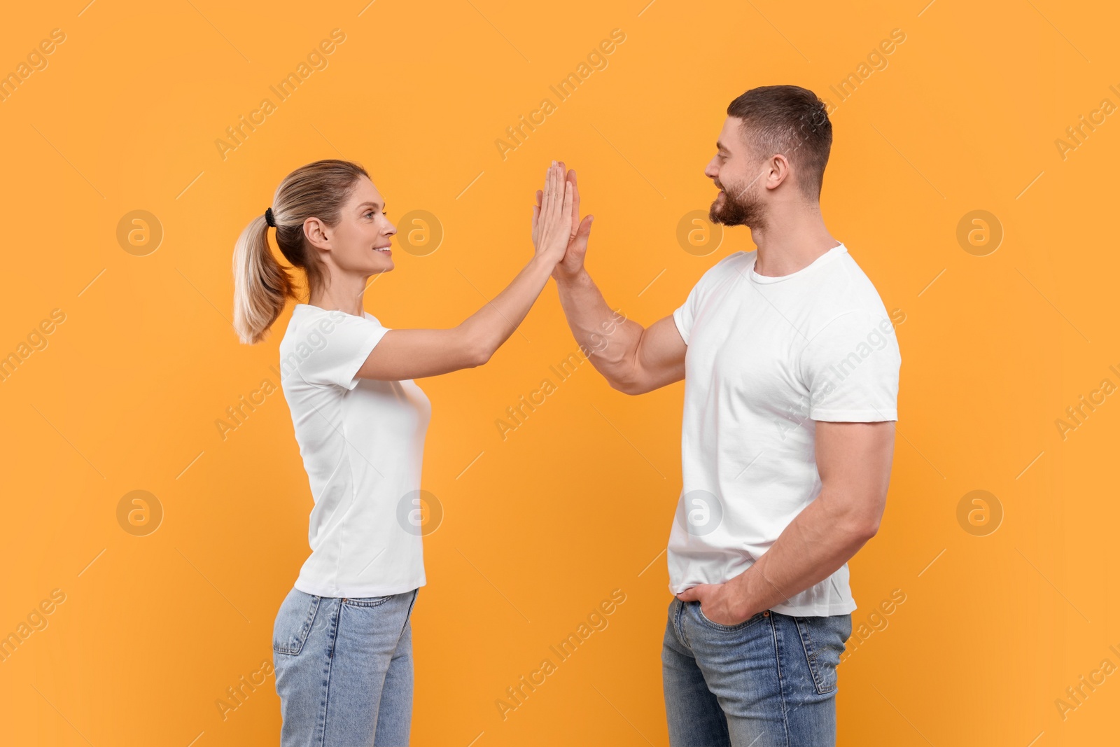 Photo of Happy couple giving high five on orange background