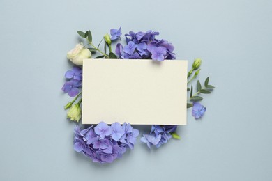 Beautiful composition with hortensia flowers and blank card on dusty light blue background, top view. Space for text