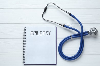 Photo of Notebook with word Epilepsy and stethoscope on white wooden table, flat lay