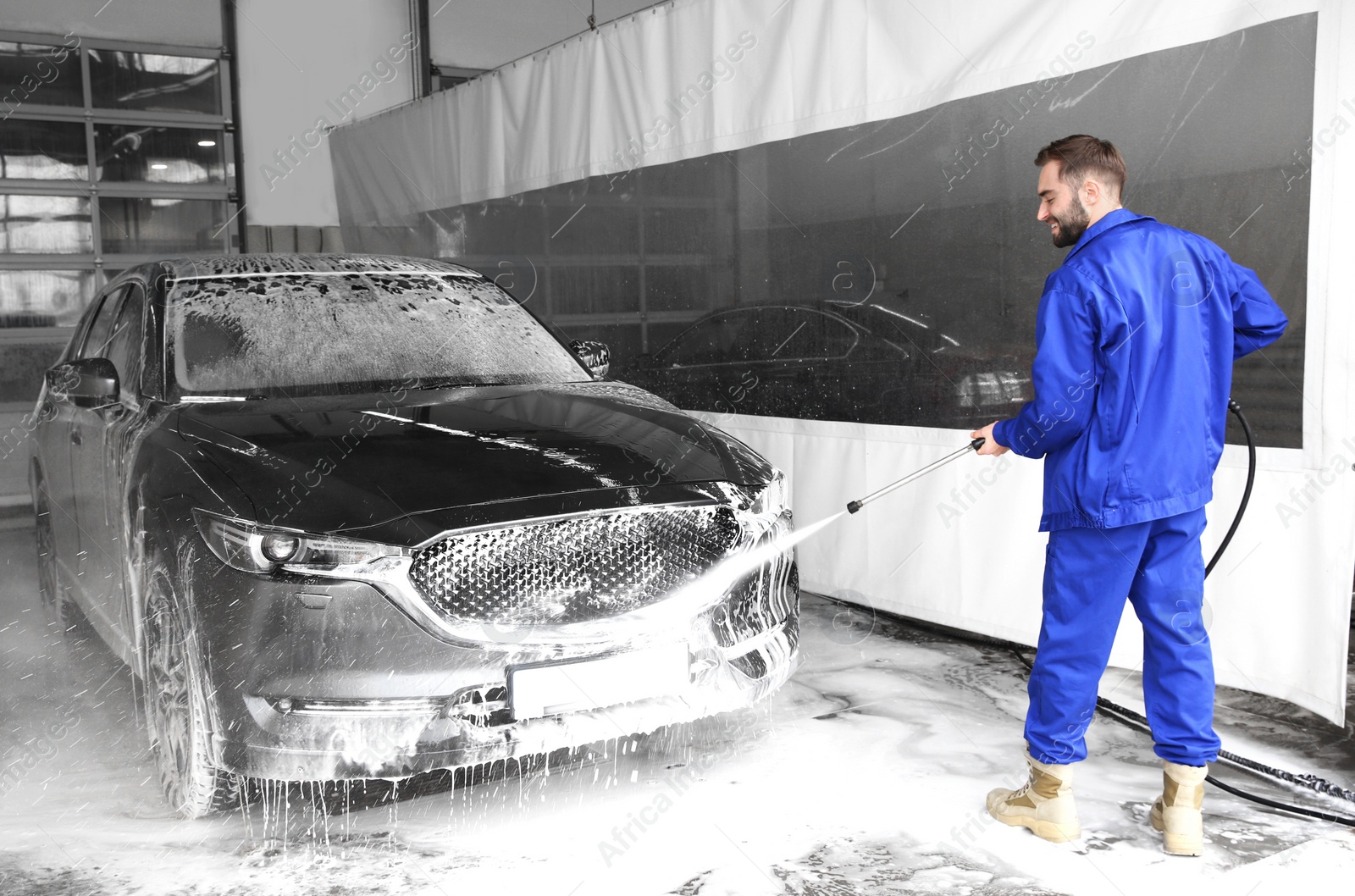 Photo of Worker cleaning automobile with high pressure water jet at car wash