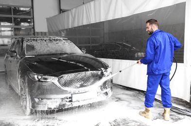 Worker cleaning automobile with high pressure water jet at car wash