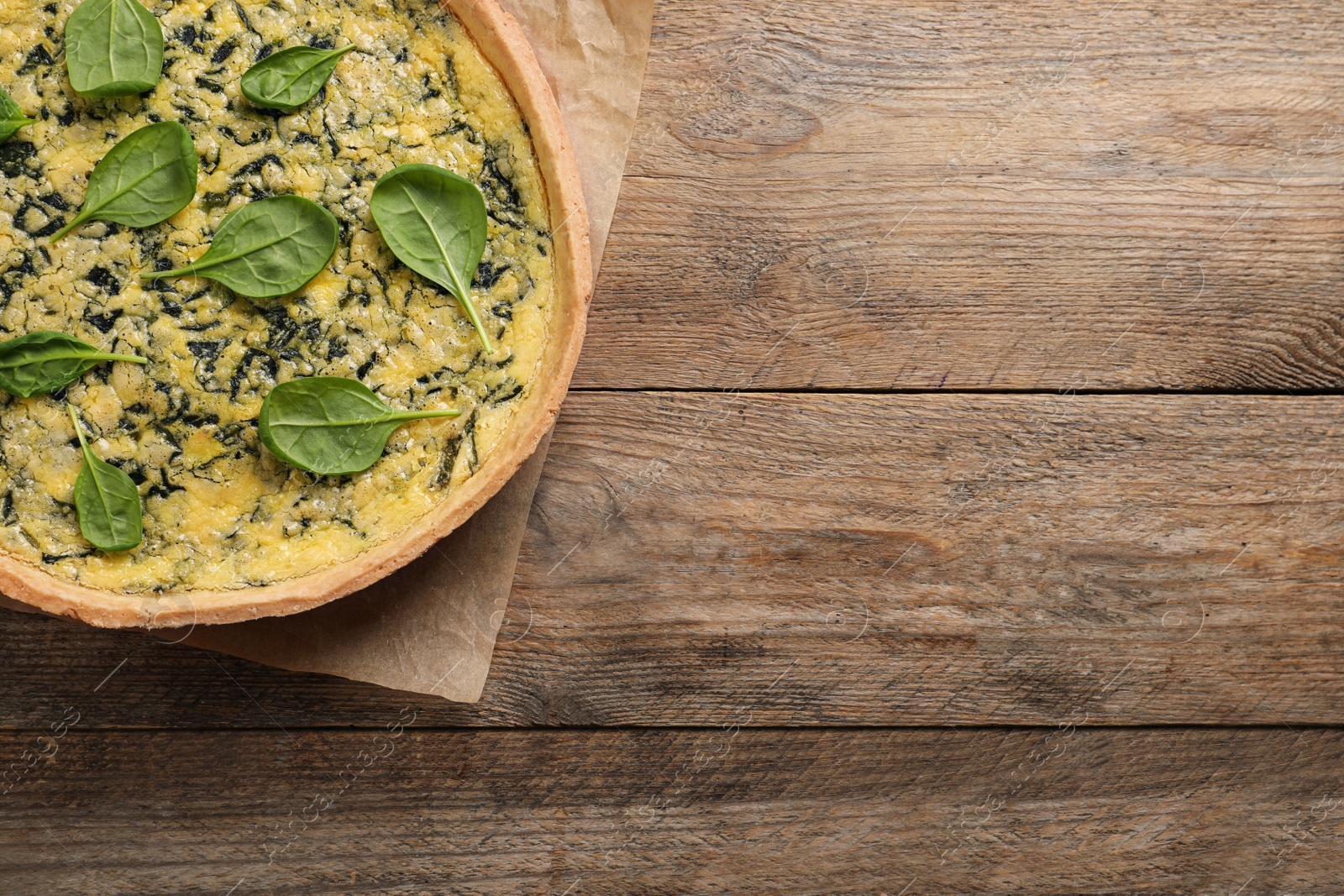 Photo of Delicious homemade spinach pie on wooden table, top view. Space for text