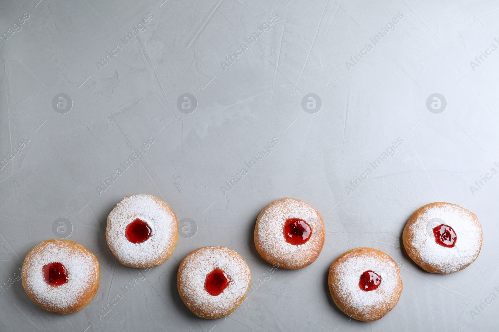 Photo of Hanukkah doughnuts with jelly and sugar powder on grey background, flat lay. Space for text