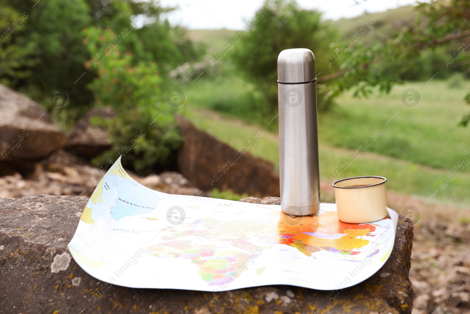 Photo of Mug, thermos and map on rock outdoors. Camping season