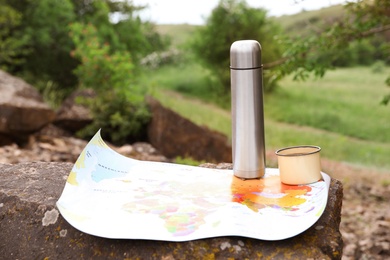 Mug, thermos and map on rock outdoors. Camping season