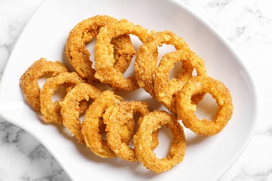 Plate with homemade crunchy fried onion rings on marble table, top view