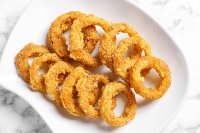 Photo of Plate with homemade crunchy fried onion rings on marble table, top view