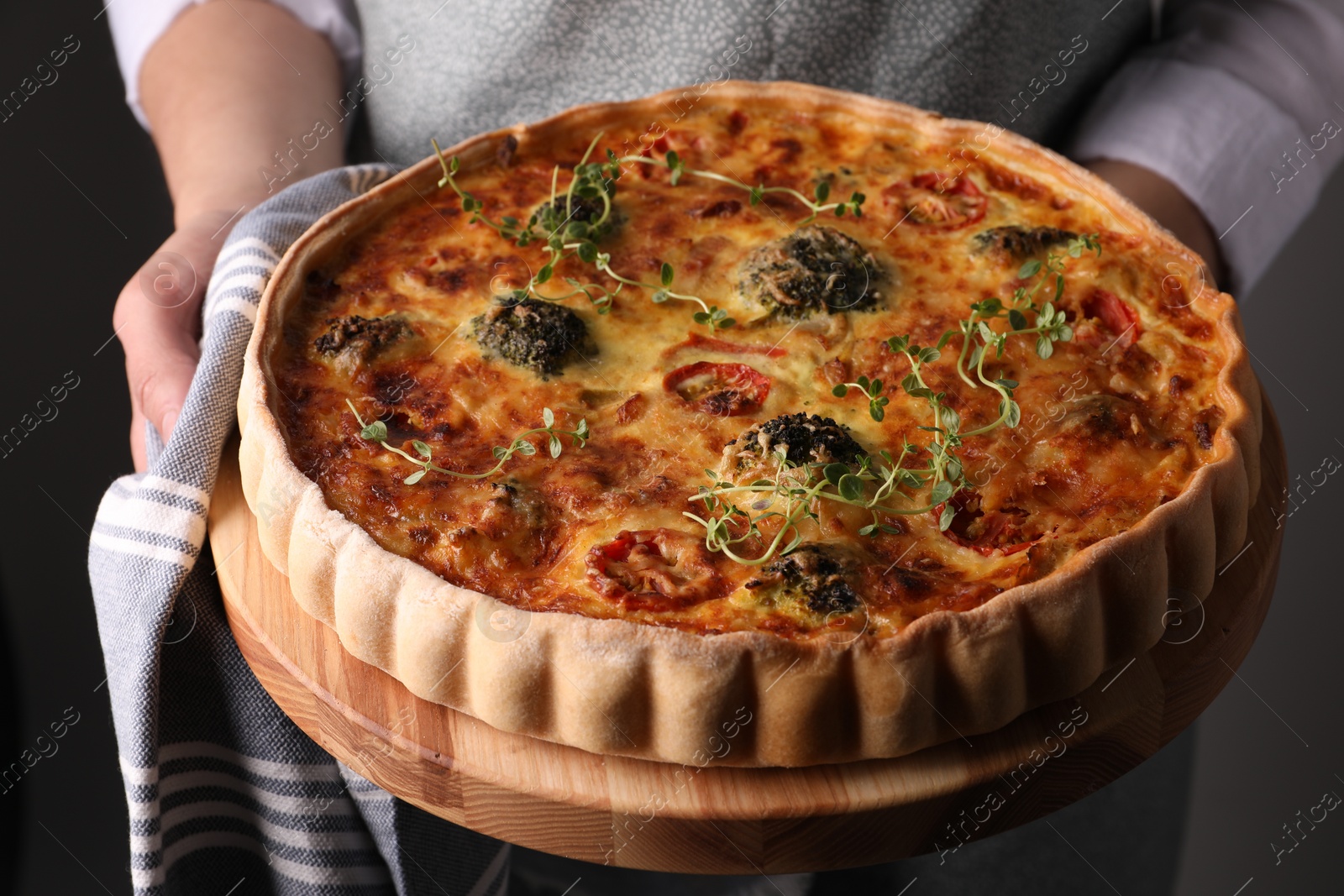 Photo of Woman holding delicious homemade vegetable quiche on black background, closeup