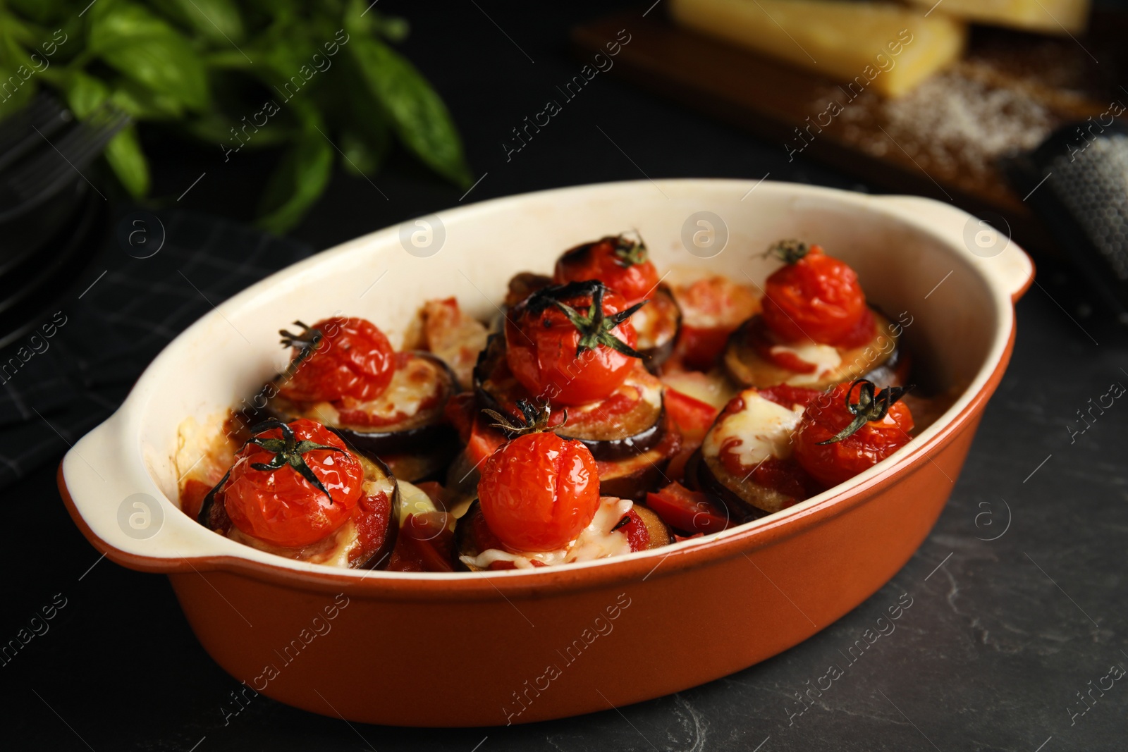Photo of Baked eggplant with tomatoes and cheese in dishware on black table