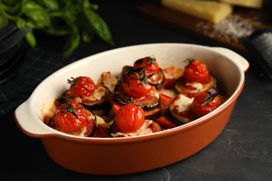 Baked eggplant with tomatoes and cheese in dishware on black table