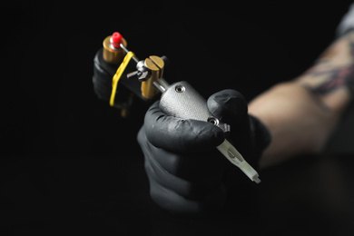 Photo of Tattoo artist with professional machine at table against black background, closeup