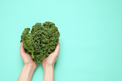 Woman holding fresh kale leaves on turquoise background, top view. Space for text