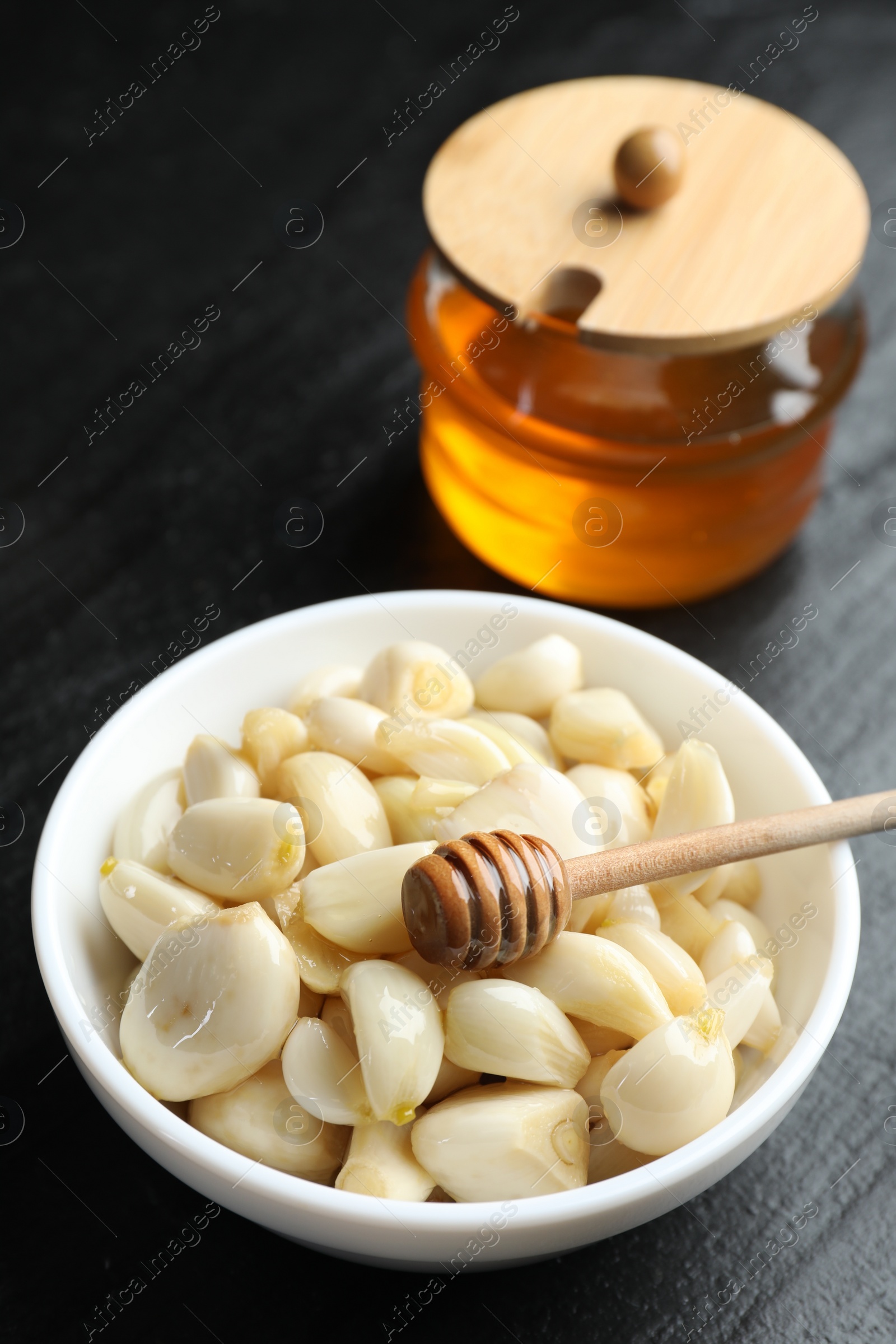 Photo of Peeled garlic cloves in bowl and honey on black table