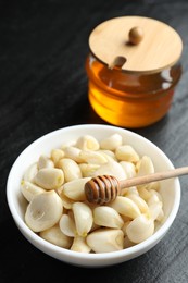 Peeled garlic cloves in bowl and honey on black table